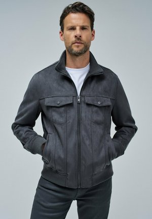 Chaqueta de ante gris con cierre de cremallera en la parte delantera, puños y dobladillo acanalados. Presenta dos bolsillos en el pecho con botones de presión y un diseño de cuello alto.
