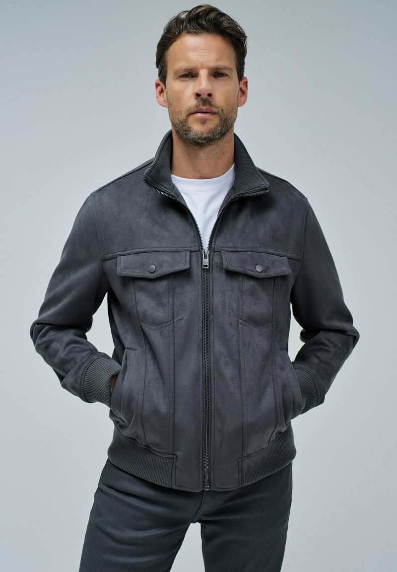 Chaqueta de ante gris con cierre de cremallera en la parte delantera, puños y dobladillo acanalados. Presenta dos bolsillos en el pecho con botones de presión y un diseño de cuello alto.