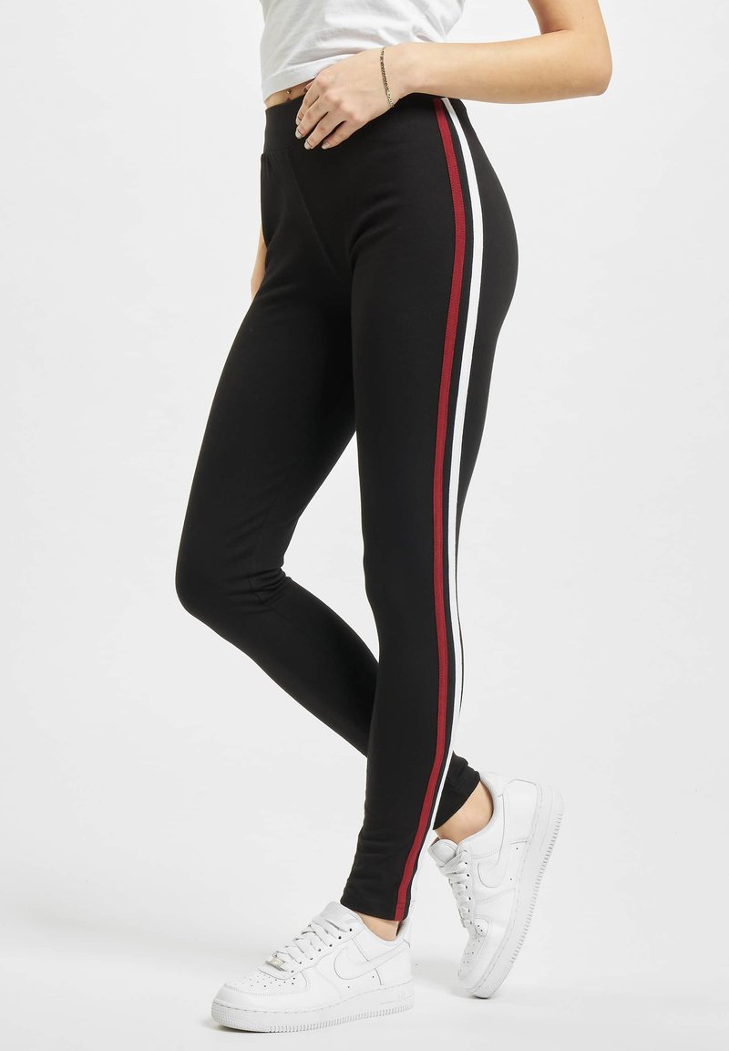 Sorte leggings med røde og hvide sidelister, lavet af strækbart materiale med en tætsiddende design, parret med hvide sneakers.