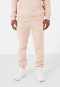 Beige fleece hoodie met een kangoeroezak, gecombineerd met bijpassende sweatpants met een elastische tailleband en cuffed hems. Witte sneakers.