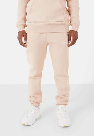 Beige fleece hoodie met een kangoeroezak, gecombineerd met bijpassende sweatpants met een elastische tailleband en cuffed hems. Witte sneakers.