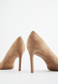 Décolleté in camoscio beige con punta affilata e tacco a stiletto sottile, caratterizzate da una texture liscia e un marchio minimale sull'intersuola.