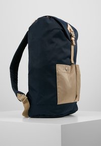 Niebieski i beżowy plecak nylonowy z boczną kieszenią, regulowanym paskiem i gładką strukturą, z detalem na zatrzask.