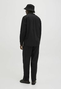 Maglietta nera a maniche lunghe e pantaloni larghi realizzati in tessuto testurizzato. Indossati con un cappello a secchiello nero con motivo e sandali piatti.