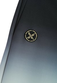 Tela negra con un parche bordado redondo que presenta un diseño circular y líneas estilizadas en hilo beige.