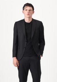 Completo a righe sottili nere con una vestibilità su misura; giacca a due bottoni, rever a punta e pantaloni a gamba dritta abbinati a una t-shirt nera semplice.