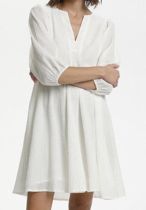 Biała sukienka z dekoltem w kształcie litery V, trzy czwarte rękawów z bufkami oraz zwiewnym, teksturowanym materiałem, posiadająca pionowe paski i sylwetkę w kształcie litery A.