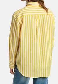 Camicia a maniche lunghe con schiena divisa, caratterizzata da strisce verticali gialle e bianche. Realizzata in cotone morbido, ha polsini con bottoni e una vestibilità rilassata.