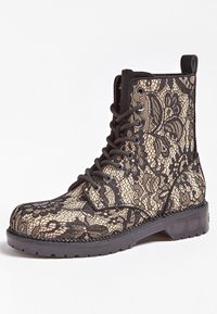 Bottes à lacets dotées d'une superposition de dentelle noire sur un fond beige, avec une surface texturée, un talon noir uni et une semelle en caoutchouc pour une meilleure traction.