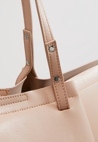 Sac fourre-tout en simili cuir rose clair avec une texture lisse, double poignées fixées par des boutons-pression argentés et détails de couture visibles.