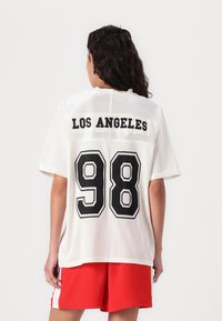 Maillot en mesh blanc avec "LOS ANGELES" imprimé au-dessus du numéro "98" en noir gras, doté de manches courtes et d'une coupe décontractée.