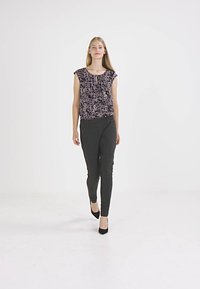 Calças pretas ajustadas combinadas com uma blusa de manga curta de flores escuras, com decote redondo e ligeiras pregas à frente.
