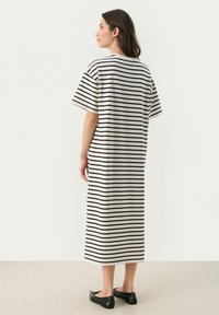 Robe midi rayée en crème et noir avec des manches courtes, une coupe ample et un col rond. Portée avec des ballerines noires.