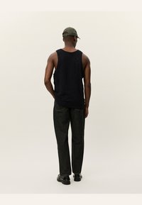 Svart ermeløs tanktop med teksturert mønster, kombinert med løstsittende mørk denimjeans og svart fottøy. Bakvisning, minimale detaljer.
