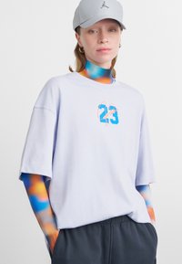 Svetlo fialové bavlnené tričko s voľným strihom, na prednej strane s modro-ružovou grafikou "23" a textom "Jordan". Sivá čiapka s logom.