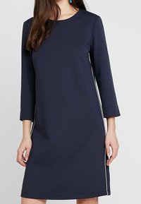 Abito blu navy con scollo rotondo e maniche a tre quarti. Presenta dettagli bianchi sottili sui lati. Tessuto morbido e vestibilità rilassata.