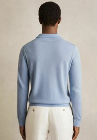 Hellblaues Strickpullover mit langen Ärmeln und ribbeltem Kragen. Glatte Textur mit einer taillierten Silhouette, kombiniert mit cremefarbenen Hosen.