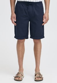 Pantaloni scurți bleumarin, până la genunchi, cu talie cu șnur, tivuri pliate și buzunare laterale. Confecționați dintr-un material ușor, cu o textură netedă.