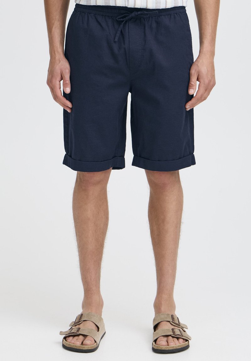 Pantaloni scurți bleumarin, până la genunchi, cu talie cu șnur, tivuri pliate și buzunare laterale. Confecționați dintr-un material ușor, cu o textură netedă.