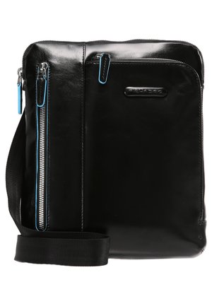 Bolsa mensajera de cuero negro con textura suave, que cuenta con dos bolsillos con cremallera y tiradores de cremallera en azul contrastante. Incluye una correa ajustable.
