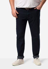 Tummansiniset farkut suoran leikkauksen omaavina, joissa on käärityt lahkeet ja hieno rakenne. Yhdistetty vaaleankreemivärisiin lenkkareihin.