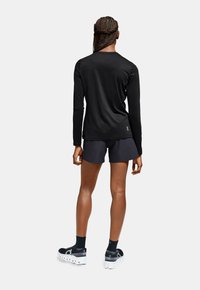 Black long-sleeve shirt with a textured finish, paired with dark shorts and black shoes featuring a white sole. Visible logo on shirt.