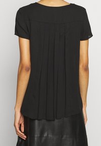 Top nero plissettato con maniche corte e scollatura rotonda, caratterizzato da cuciture verticali per aggiungere texture e fluidità.