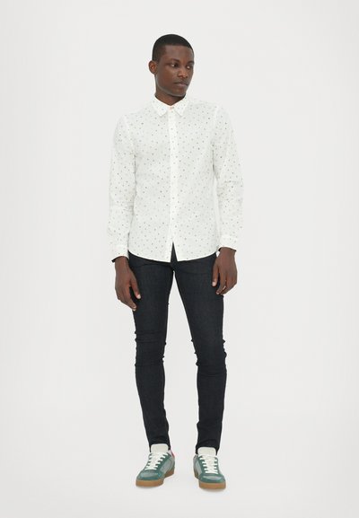 White button-up shirt with multicolored tiny dots, paired with fitted black jeans and green sneakers with white laces and tan soles.