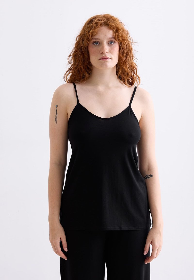 Zwarte camisole met dunne bandjes, gemaakt van zachte stof. Heeft een V-hals ontwerp en een losse pasvorm, gecombineerd met zwarte wijde broeken.