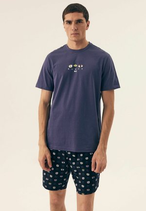 Fioletowy bawełniany t-shirt z graficznym wzorem sushi. W połączeniu z czarnymi szortami z kolorowym wzorem sushi. Luźny krój.