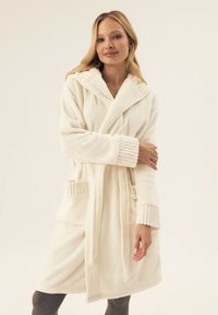 Kremowy polarowy szlafrok z kapturem, ribbowane mankiety i dwie przednie kieszenie. Miękka tekstura i średniej długości fason.