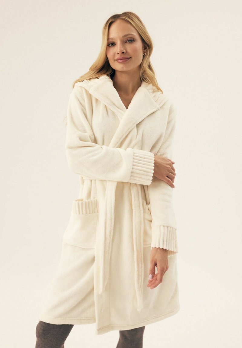 Kremowy polarowy szlafrok z kapturem, ribbowane mankiety i dwie przednie kieszenie. Miękka tekstura i średniej długości fason.