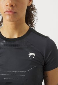 Svart trenings t-skjorte med korte ermer, med et strukturert mønster og en hvit logo. Glatt materiale og tettsittende design.