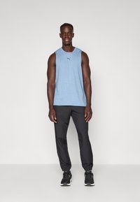 Lichtblauw mouwloos sporttanktop met een vage textuurlijn; gecombineerd met zwarte broek en zwarte sneakers met groene accenten.