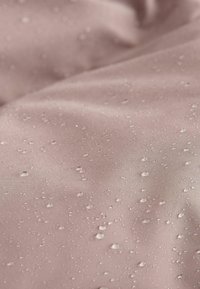 Tissu résistant à l'eau en rose doux, présentant une texture lisse avec des gouttes d'eau disséminées, mettant en avant sa qualité imperméable.