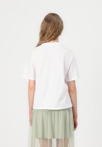 T-shirt en coton blanc à col arrondi, associé à une jupe en tulle vert clair. Le t-shirt a des manches courtes et une coupe décontractée.