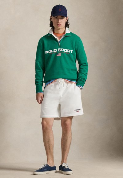 Πράσινη φούτερ μπλούζα με λευκό γιακά και λογότυπο «POLO SPORT», λευκά σορτς με κορδόνι και ναυτικά αθλητικά παπούτσια. Καθημερινό ντύσιμο με πολλαπλά στρώματα.