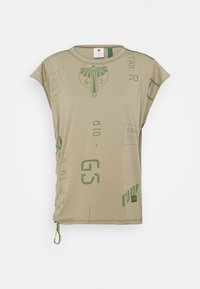 Beige sleeveless top with green abstract symbols, text prints, and a small fabric tag near the hem on a white background.