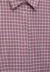 Chemise à carreaux en violet clair et blanc. Tissu en coton avec col boutonné et boutons violets. Présente de petits motifs carrés sur toute la surface.