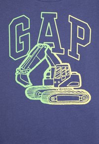 T-shirt bleu avec un graphisme d'une excavatrice en vert et jaune, avec le mot "GAP" affiché en lettres majuscules en gras au-dessus.