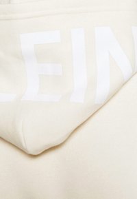 Primo piano di un tessuto beige chiaro con grandi lettere bianche parzialmente visibili che dicono "LEIN" stampate sulla superficie.