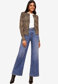 Kardigan s leopardjim uzorkom u bež i crnoj boji, uparen s belim topom i farmericama sa visokim strukom i širokim nogavicama u plavoj boji. Crne štikle s oštrim vrhom.