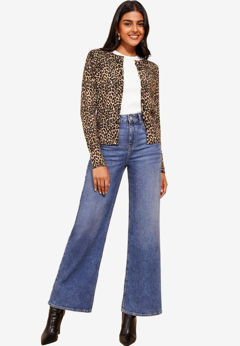 Kardigan s leopardjim uzorkom u bež i crnoj boji, uparen s belim topom i farmericama sa visokim strukom i širokim nogavicama u plavoj boji. Crne štikle s oštrim vrhom.