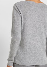 Hellgrauer Pullover aus weichem Stoff mit rundem Halsausschnitt und gerippten Bündchen. Am Rücken befindet sich ein dezentes Designdetail am Nacken.