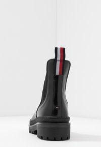 Musta nilkkuri, jossa on sileä nahkapinta ja teksturoitu sivupaneeli. Varustettu monivärisellä raidallisella vetonauhalla ja paksulla kumipohjalla.