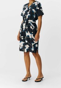 Kurzärmliges, knielanges Kleid aus dunklem Stoff mit abstrakten Mustern in Weiß und Blau; mit durchgehender Knopfleiste und Taillengürtel.