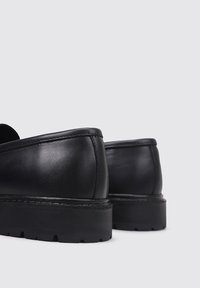 Zapatos de cuero negro con un acabado suave y brillante y una suela de goma gruesa y texturizada. Diseño de punta redondeada con detalles de costura mínimos.