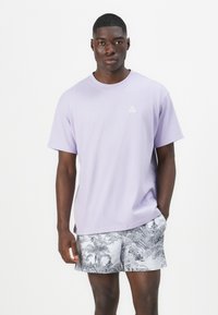 Light purple cotton t-shirt with short sleeves and crew neck, featuring a small white logo on the chest, paired with patterned gray shorts.