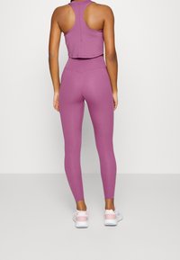 Paarse geknipte tanktop gecombineerd met hoogtaille paarse legging. De sportkleding heeft een gladde textuur en een aansluitend ontwerp.