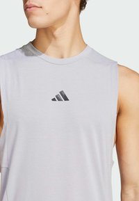 Ärmlös ljusgrå träningsskjorta med rund krage och en svart Adidas-logotyp på bröstet, tillverkad av ett slätt, luftigt tyg.